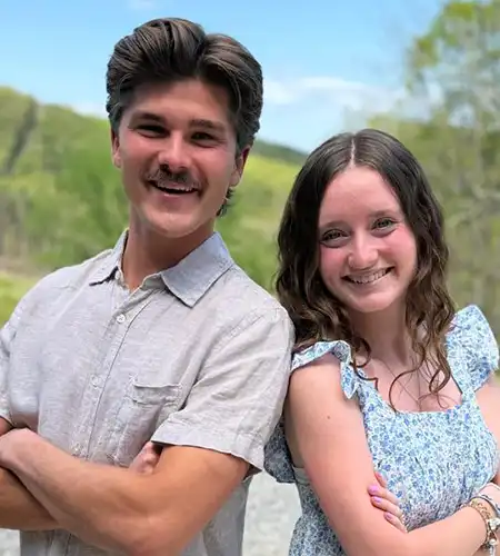 Two people smiling while posing outdoors in a sunny, green park setting.